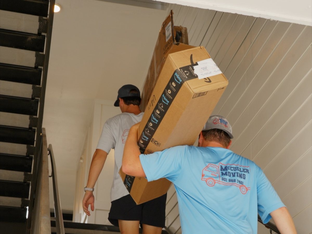 McCuller Moving crew carrying a boxed furniture delivery up an apartment stairwell
